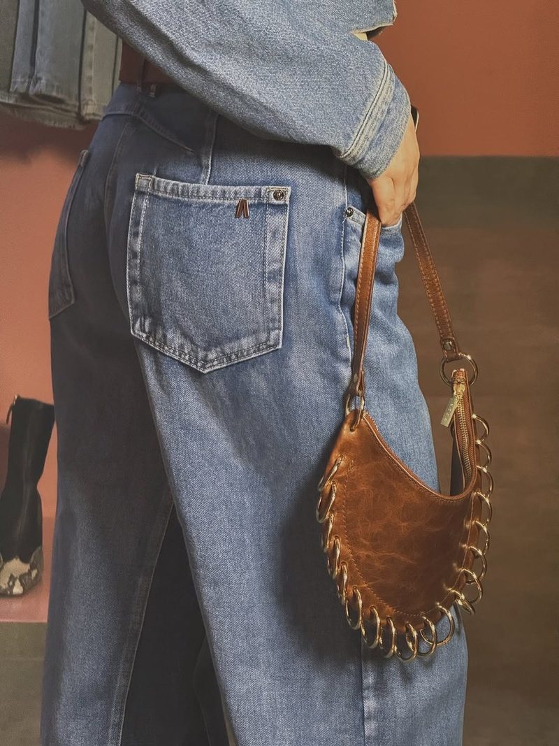 Detalhe do bolso traseiro de uma calça jeans com bolsa meia-lua de couro